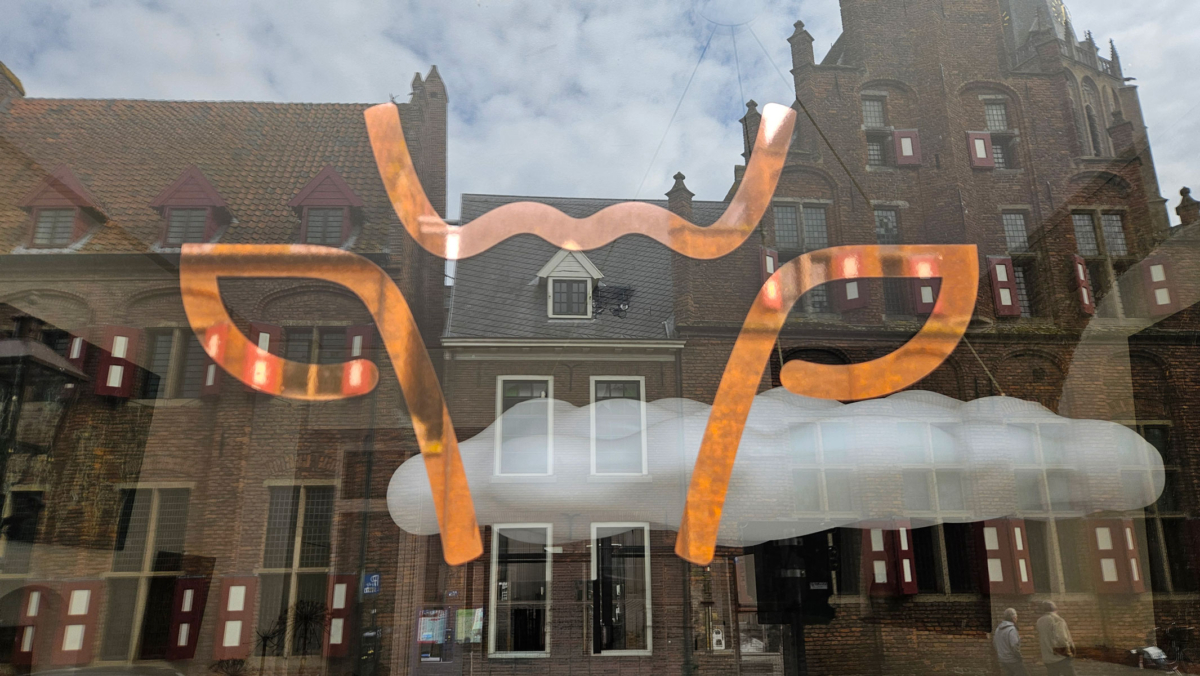 Raam van Studio Koepoort met koperkleurige belettering en zicht naar binnen door het glas