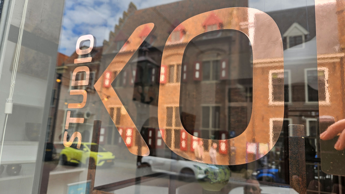 Close-up van koperfolie belettering op het raam van Studio Koepoort met fijne structuur en glans