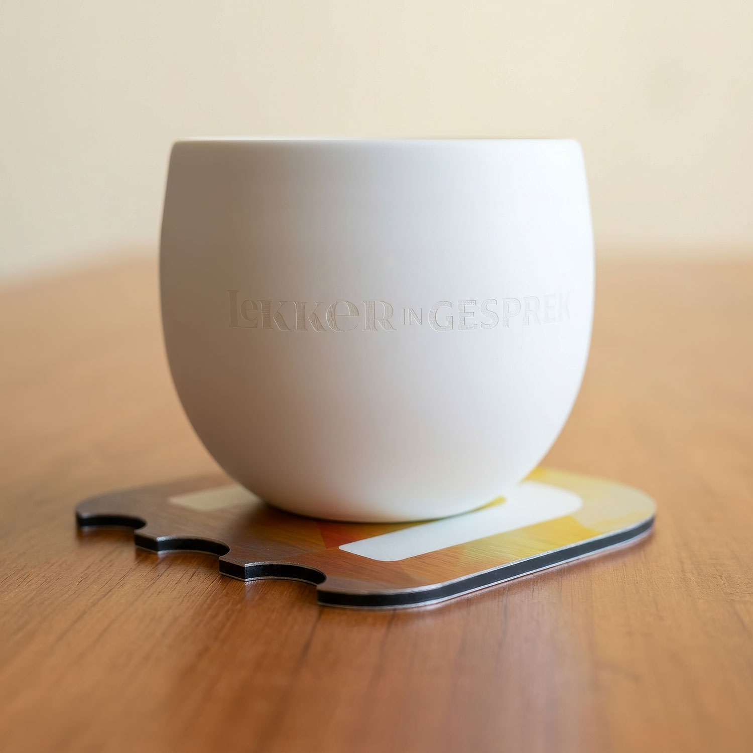 Een koffiekopje dat op een bedrukte onderzetter van Uitgerekend Hier staat.