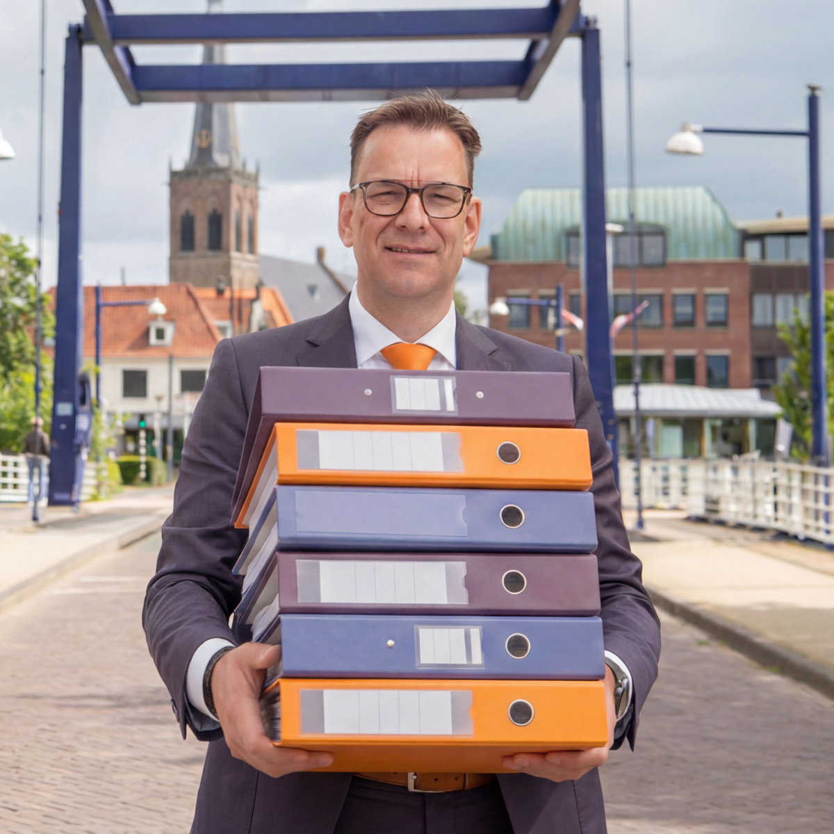 Uitgerekend Hier in de Doetinchemse binnenstad René van Uitgerekend Hier met ordners in de huisstijlkleuren op de brug in de Doetinchemse binnenstad.